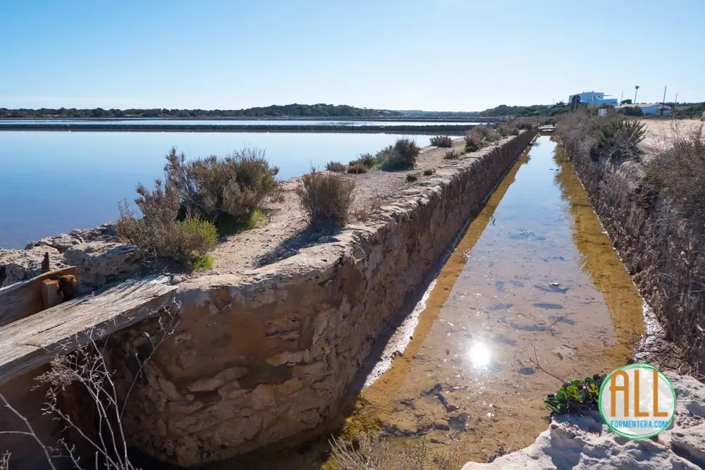 Canales para inundar las lagunas de las salinas de Formentera. El canal tiene algo de agua en su interior y el sol se refleja en ella.