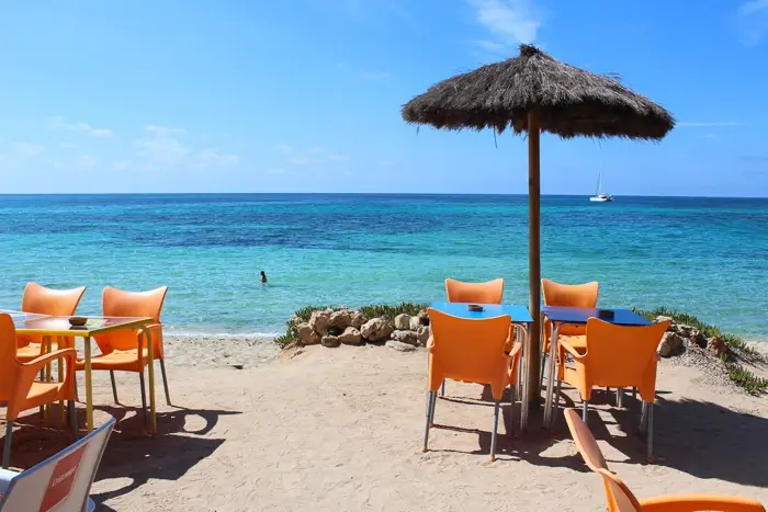 Tables dans un bar de plage à Formentera avec la mer en arrière-plan et une fille dans l'eau.